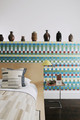 Christopher Farr textile collection featuring Anni Albers’ Child’s Check wallpaper alongside Black Mountain fabric showcased as a cushion and bedspread, blending iconic geometric patterns in a modern interior setting.